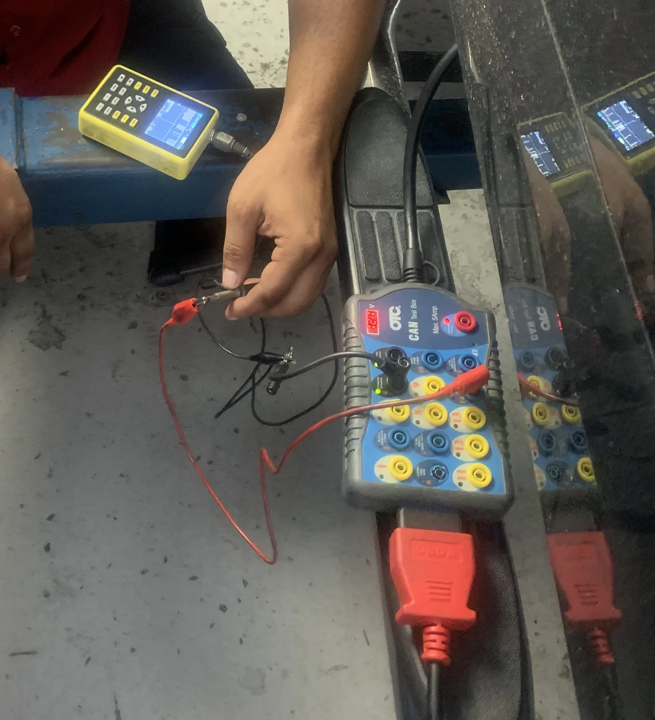OTC CAN test box breakout adapter connected at the OBD-II port with test leads and a handheld oscilloscope displaying a waveform, during network diagnosis at RepairTech Automotive in Kissimmee