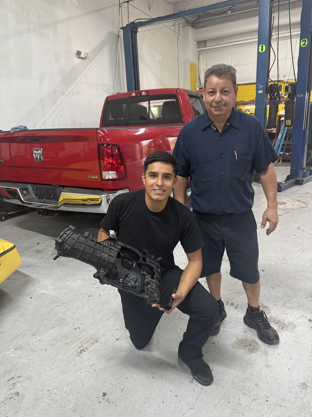 Two RepairTech Automotive technicians in the Kissimmee shop holding an intake manifold removed from a customer's truck, showing heavy carbon buildup